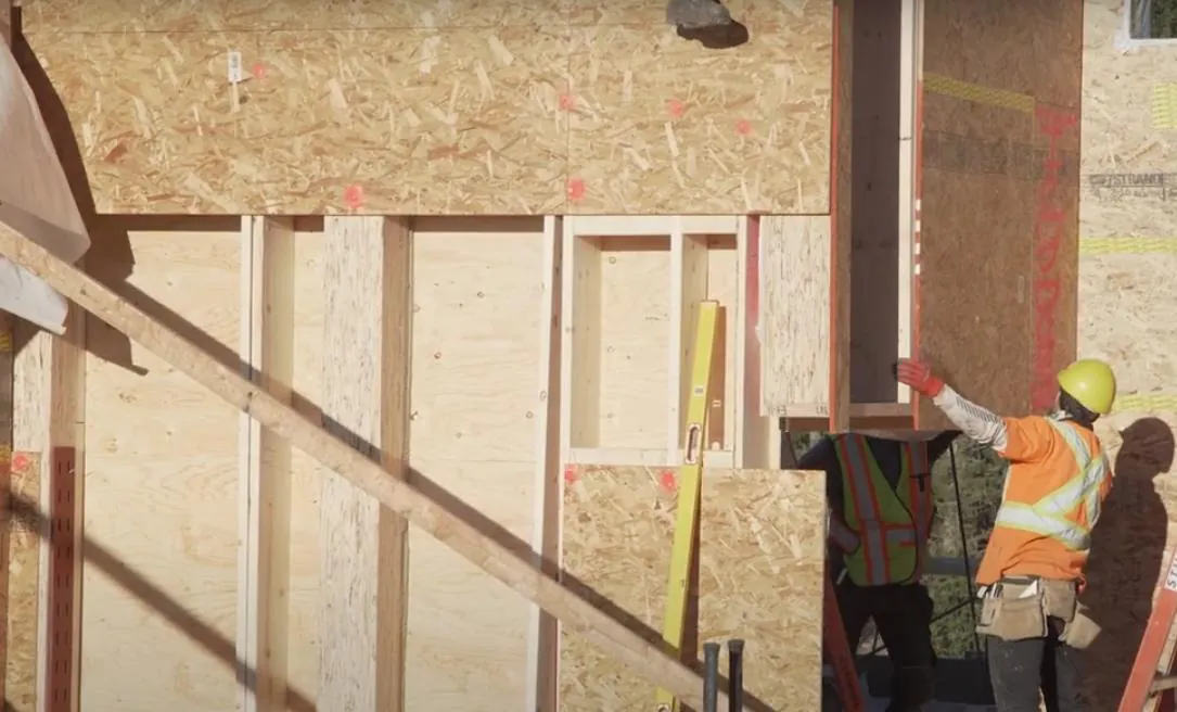 Installers positioning a prefabricated insulated wall panel onto the floor structure on site